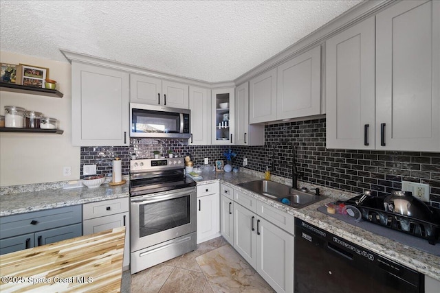 kitchen featuring a sink, backsplash, appliances with stainless steel finishes, a textured ceiling, and open shelves