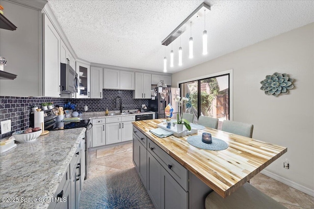 kitchen with butcher block countertops, a breakfast bar, a sink, stainless steel appliances, and decorative backsplash