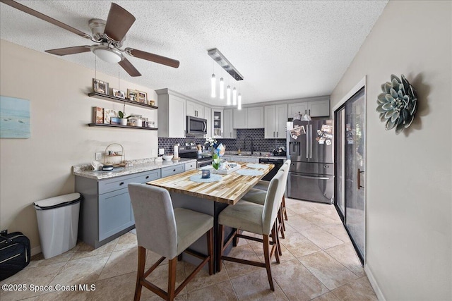 kitchen featuring gray cabinetry, ceiling fan, appliances with stainless steel finishes, a textured ceiling, and tasteful backsplash