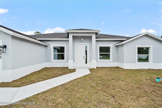 view of front of property featuring stucco siding, a front yard, and a shingled roof