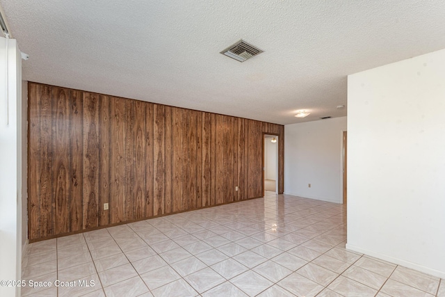 spare room with light tile patterned floors, visible vents, wooden walls, and a textured ceiling