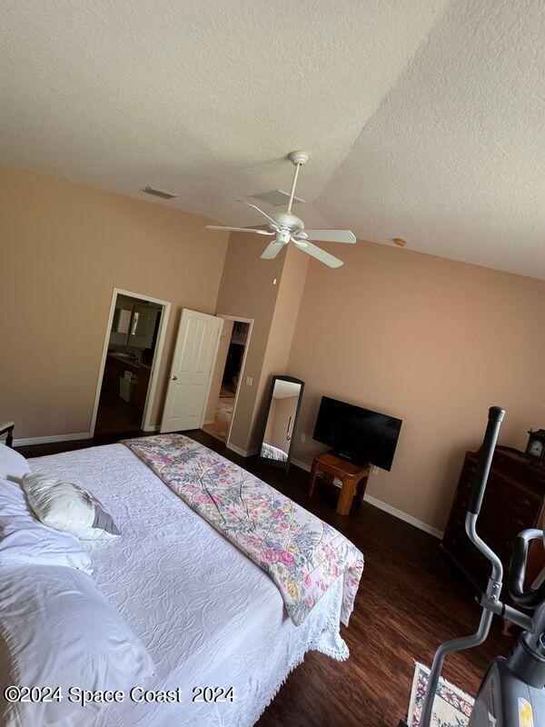 bedroom with lofted ceiling, a textured ceiling, wood finished floors, baseboards, and ceiling fan