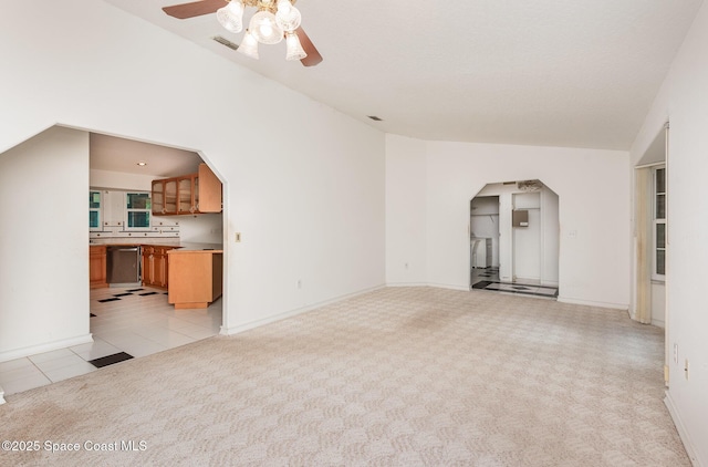 unfurnished living room featuring arched walkways, light colored carpet, light tile patterned flooring, and a ceiling fan