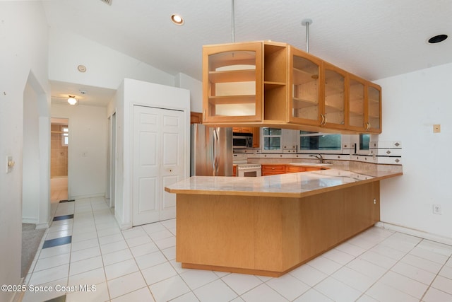 kitchen with light tile patterned flooring, a peninsula, stainless steel appliances, and glass insert cabinets