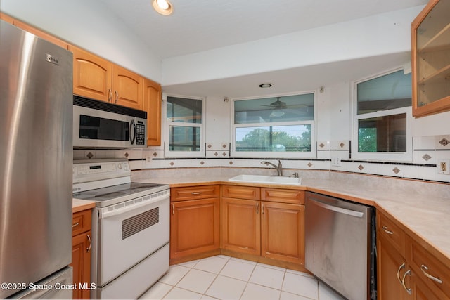 kitchen featuring a sink, stainless steel appliances, light countertops, glass insert cabinets, and tasteful backsplash