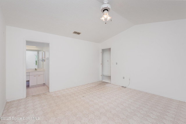 unfurnished bedroom featuring visible vents, a sink, vaulted ceiling, ensuite bathroom, and light colored carpet