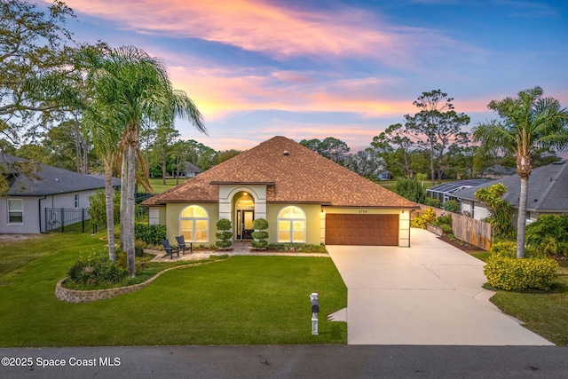 mediterranean / spanish-style home featuring stucco siding, concrete driveway, a front lawn, and fence