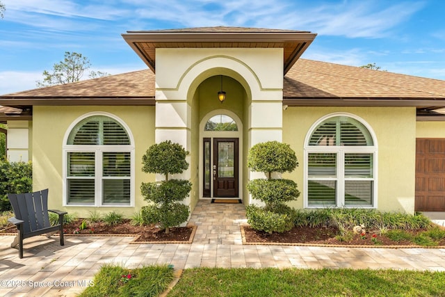 entrance to property with stucco siding, a patio area, and a shingled roof