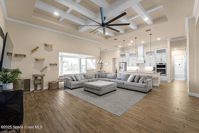 living room featuring wood finished floors, baseboards, coffered ceiling, a high ceiling, and ceiling fan with notable chandelier