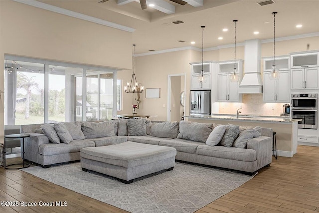 living area featuring crown molding, light wood-type flooring, recessed lighting, ceiling fan with notable chandelier, and a towering ceiling