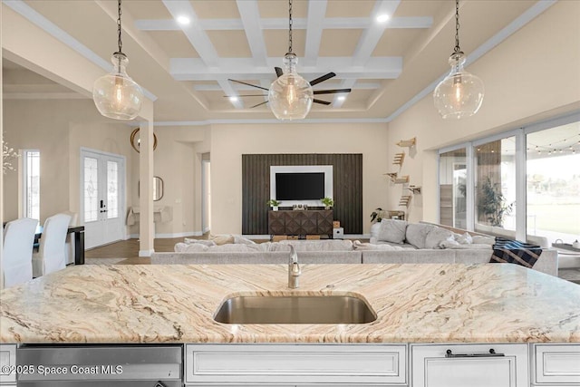 kitchen with a sink, light stone counters, coffered ceiling, open floor plan, and ceiling fan