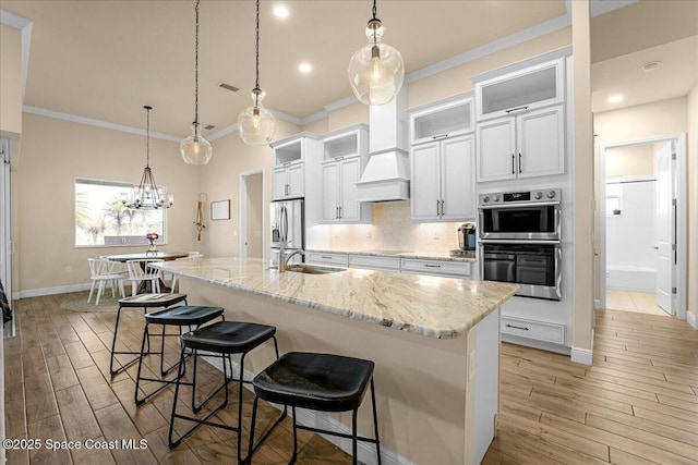 kitchen with an island with sink, a sink, stainless steel appliances, custom range hood, and backsplash