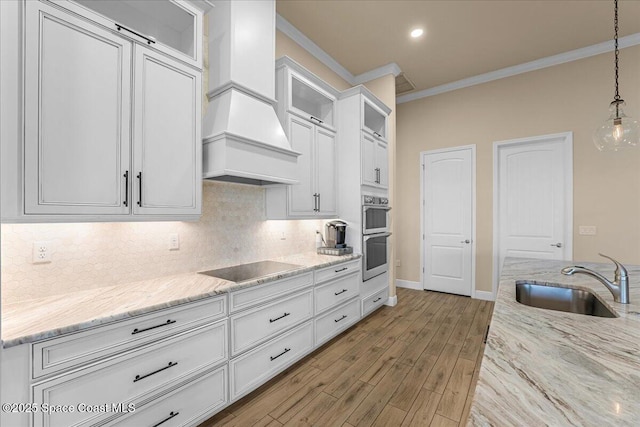 kitchen featuring a sink, custom range hood, white cabinetry, decorative light fixtures, and black electric cooktop