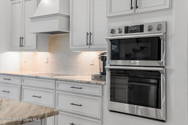 kitchen featuring premium range hood, white cabinetry, double oven, black electric cooktop, and backsplash