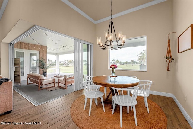 dining area with crown molding, baseboards, wood finished floors, a towering ceiling, and an inviting chandelier