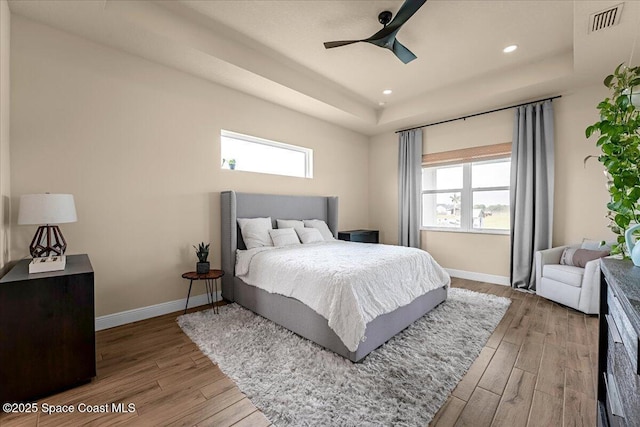 bedroom featuring multiple windows, a raised ceiling, baseboards, and wood finished floors