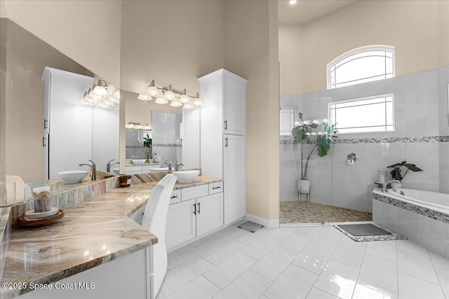 full bath featuring double vanity, a sink, a towering ceiling, walk in shower, and a garden tub