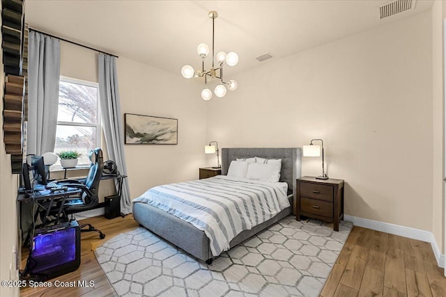 bedroom featuring an inviting chandelier, wood finished floors, and visible vents