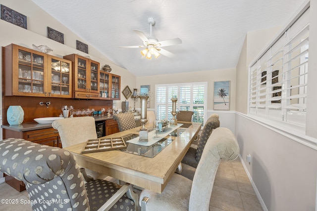 dining room with light tile patterned floors, baseboards, indoor bar, ceiling fan, and vaulted ceiling