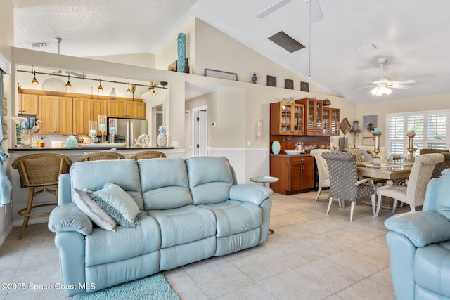 living area with light tile patterned floors, visible vents, ceiling fan, vaulted ceiling, and a textured ceiling