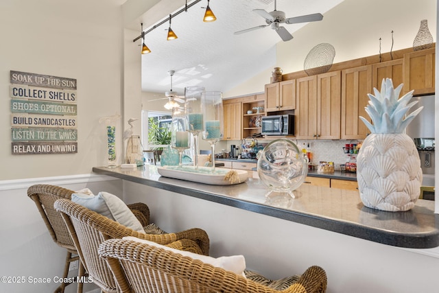 kitchen with a ceiling fan, stainless steel microwave, dark countertops, decorative backsplash, and lofted ceiling