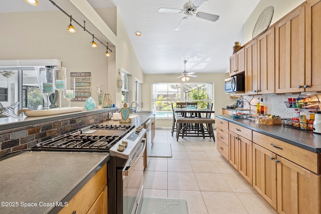 kitchen featuring dark countertops, ceiling fan, appliances with stainless steel finishes, light tile patterned flooring, and a sink