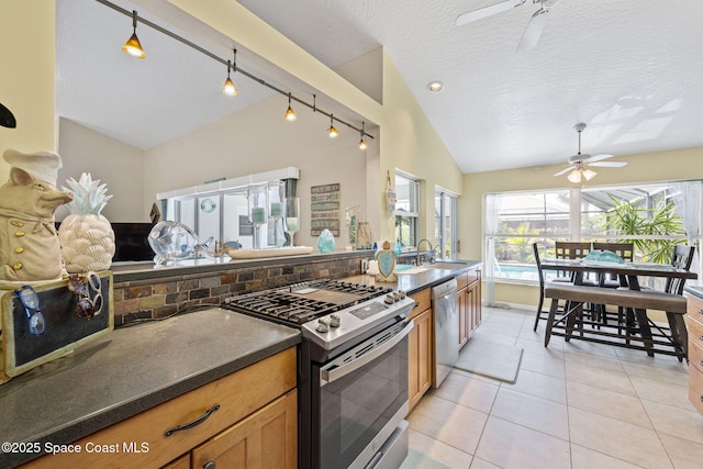 kitchen with dark countertops, lofted ceiling, stainless steel appliances, a ceiling fan, and a sink