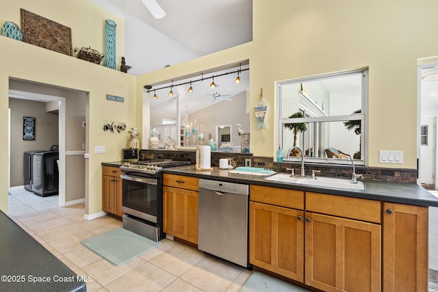 kitchen featuring dark countertops, washer and clothes dryer, appliances with stainless steel finishes, a ceiling fan, and a sink