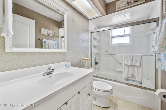 full bathroom featuring vanity, shower / bath combination with glass door, tile patterned floors, toilet, and tile walls