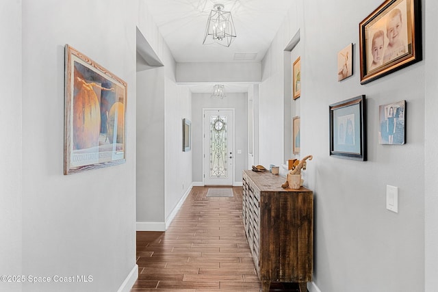 hall featuring baseboards, a notable chandelier, and wood finished floors