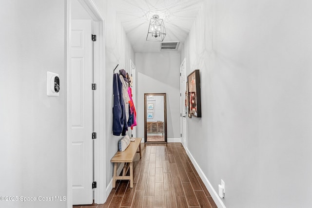 corridor featuring wood finish floors, visible vents, baseboards, and an inviting chandelier