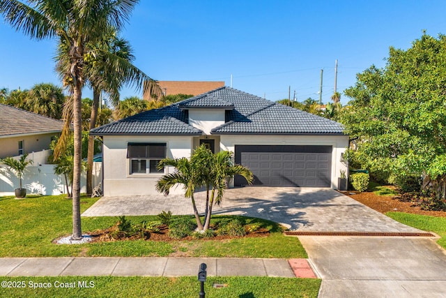 view of front of home with a front lawn, a tiled roof, stucco siding, a garage, and driveway