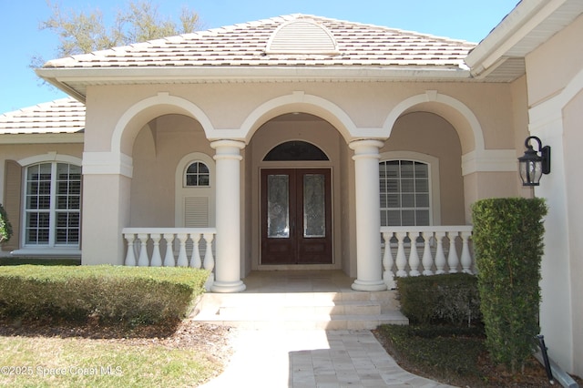 property entrance featuring a tiled roof, french doors, a porch, and stucco siding