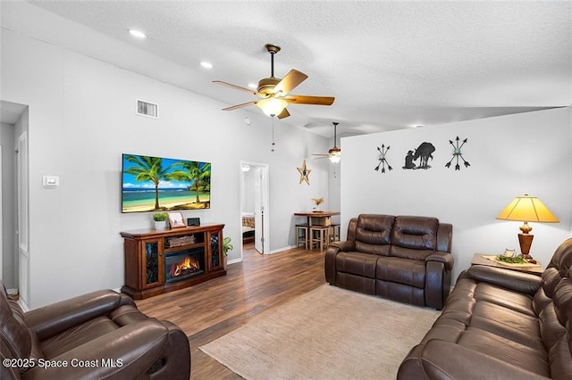 living room featuring wood finished floors, a ceiling fan, visible vents, and a textured ceiling