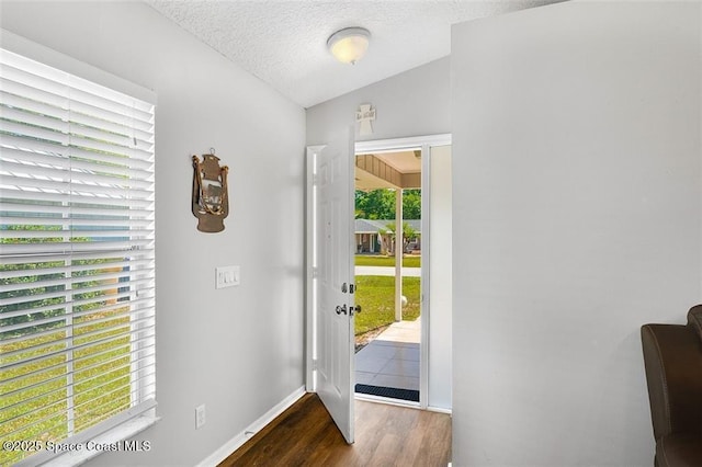 doorway to outside with lofted ceiling, wood finished floors, baseboards, and a textured ceiling