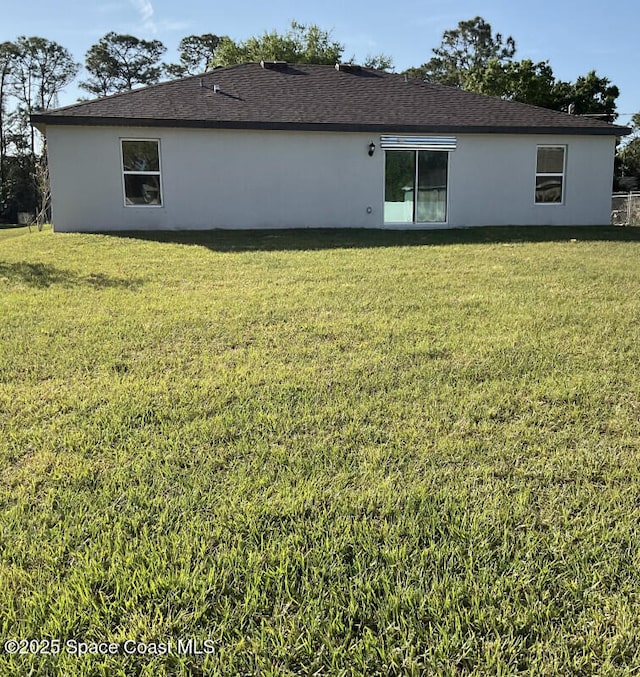 back of property with a lawn, roof with shingles, and stucco siding