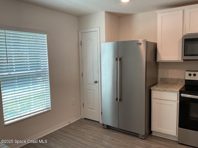 kitchen with appliances with stainless steel finishes, white cabinets, light wood finished floors, baseboards, and light stone countertops