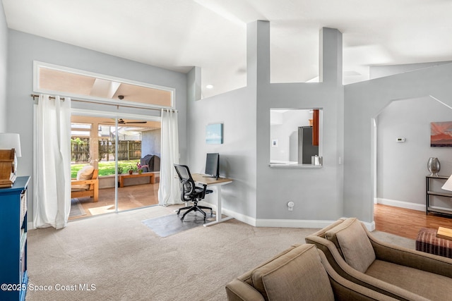 carpeted living area featuring a desk, baseboards, and arched walkways