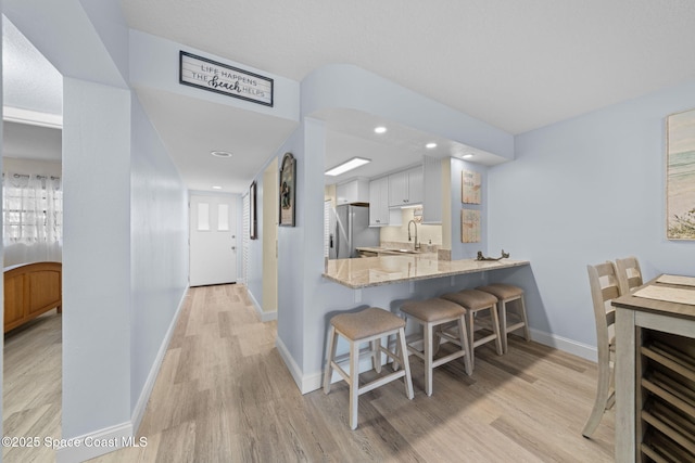 kitchen featuring a kitchen bar, light wood-type flooring, stainless steel refrigerator with ice dispenser, a sink, and light stone countertops