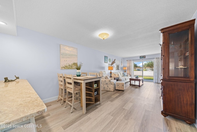 dining space with light wood finished floors, a textured ceiling, and baseboards