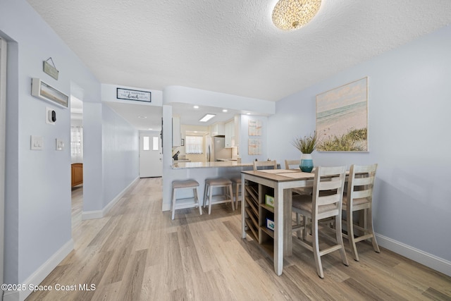 dining room featuring a textured ceiling, light wood-type flooring, and baseboards