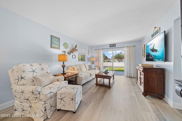 living room featuring baseboards, a textured ceiling, and light wood finished floors