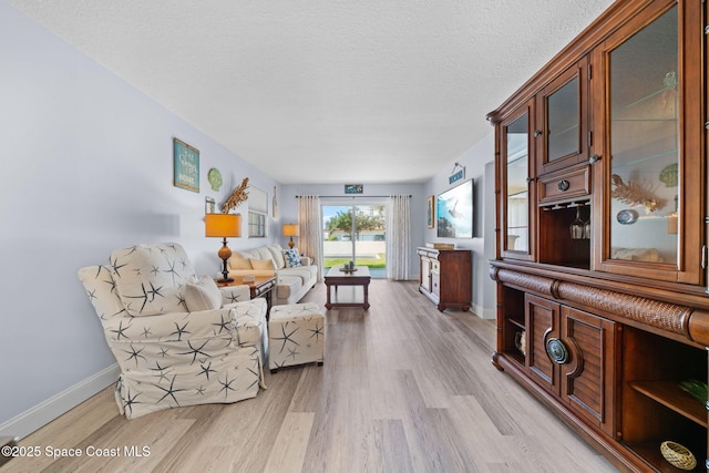 living room featuring baseboards, light wood-style floors, and a textured ceiling