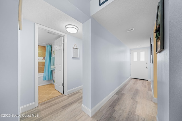 hall with visible vents, baseboards, a textured ceiling, and light wood finished floors