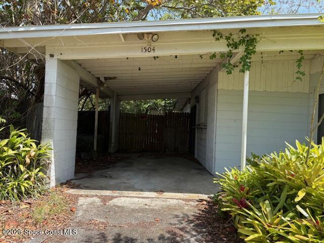 view of car parking featuring concrete driveway, fence, and a carport