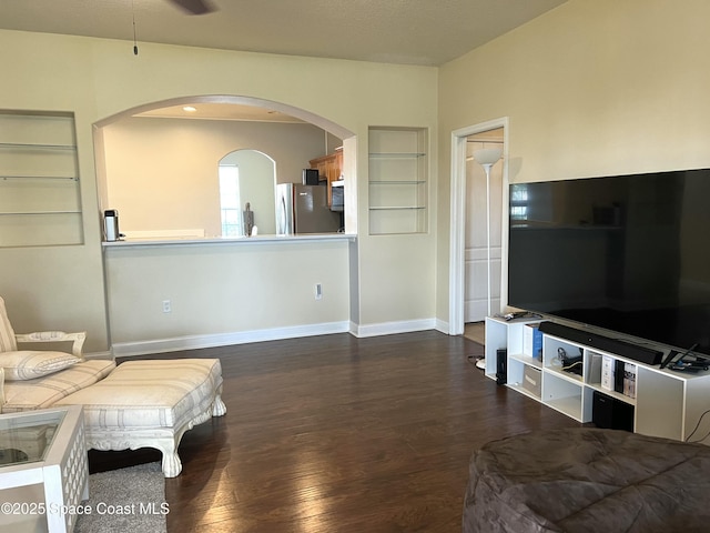 living area featuring built in features, wood finished floors, arched walkways, baseboards, and ceiling fan