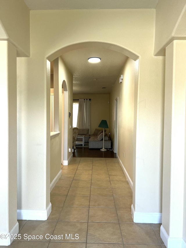 hall with arched walkways, light tile patterned floors, and baseboards