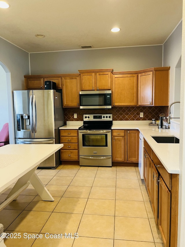 kitchen featuring arched walkways, appliances with stainless steel finishes, light countertops, and a sink