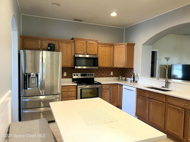 kitchen featuring visible vents, brown cabinetry, arched walkways, stainless steel appliances, and a sink