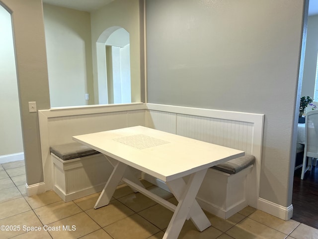 dining space featuring light tile patterned floors, baseboards, arched walkways, and breakfast area